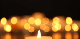 Single lit candle with blurred lights background.