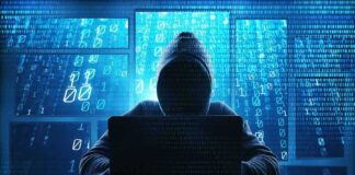 Hacker in hoodie typing on laptop with binary code.