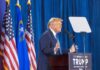 Person speaking at podium with flags in background.