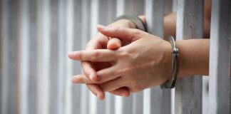 Hands in handcuffs gripping prison bars