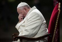 Man in white coat sitting with head in hand