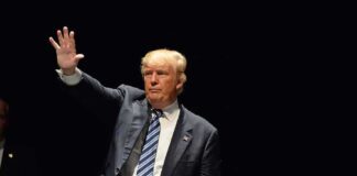 Man in a suit waving against dark background.