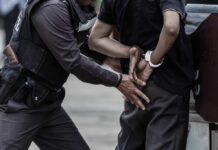 Police officer arrests person in handcuffs outdoors