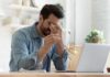 Man rubbing eyes while holding glasses near laptop
