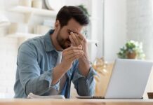 Man rubbing eyes while holding glasses near laptop