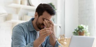 Man rubbing eyes while holding glasses near laptop