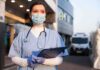 Doctor wearing mask and gloves holding clipboard outside hospital