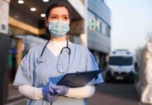 Doctor wearing mask and gloves holding clipboard outside hospital