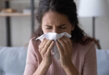 Woman sneezing into a tissue indoors