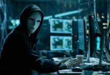Person wearing mask and hoodie at computer desk