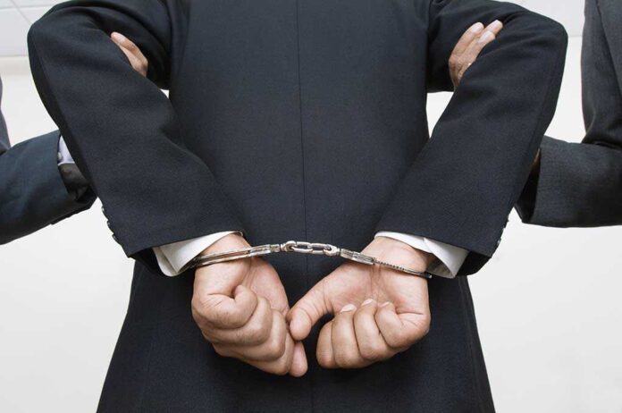 121141399 featured image Person handcuffed in suit, escorted by two others.