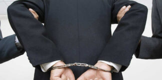 Person handcuffed in suit, escorted by two others