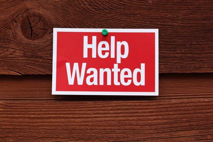 A red and white 'Help Wanted' sign pinned to a wooden surface