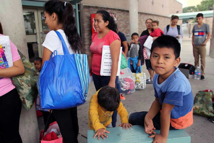 People waiting outside carrying bags, boys sitting and playing.