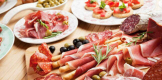 Assorted charcuterie with olives, bread, and tomatoes on plate.