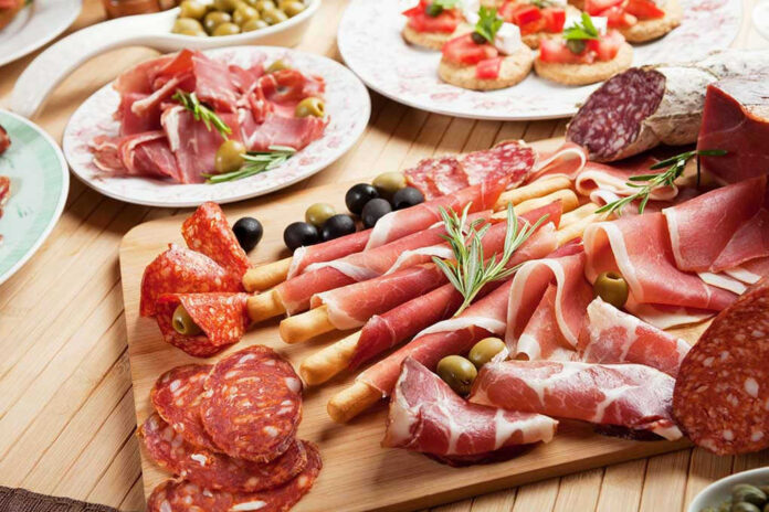 Assorted charcuterie with olives, bread, and tomatoes on plate.