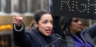 A woman passionately speaking at a rally with a sign in the background