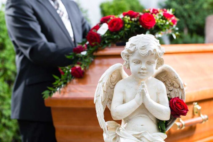 A stone angel statue with roses in front of a wooden casket at a funeral service