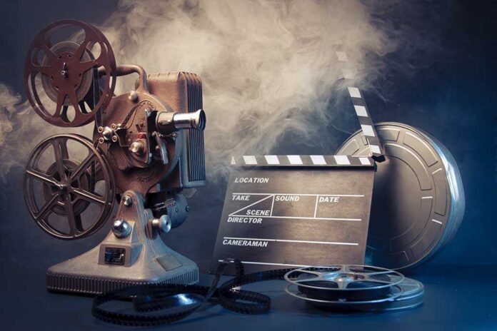 A vintage film projector with film reels and a clapperboard surrounded by smoke