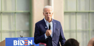 Man speaking at an outdoor event with Biden sign