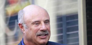 A smiling man in a suit and shirt outdoors engaged in conversation