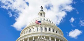 The US Capitol building with an American flag flying in front against a blue sky
