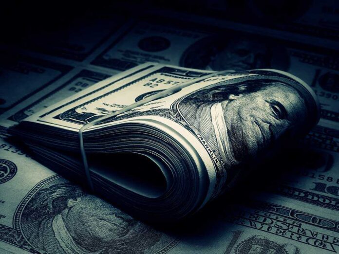 A rolled stack of hundred-dollar bills on a background of more banknotes