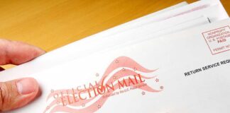 A hand holding an envelope labeled Official Election Mail