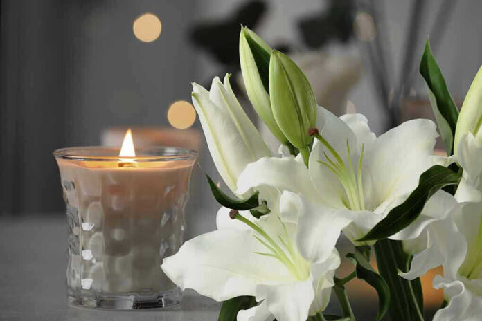 Lit candle next to white lilies.