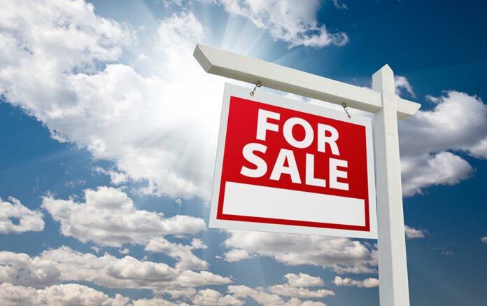 A red For Sale sign against a blue sky with clouds