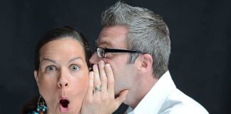 A surprised woman reacting while a man whispers in her ear