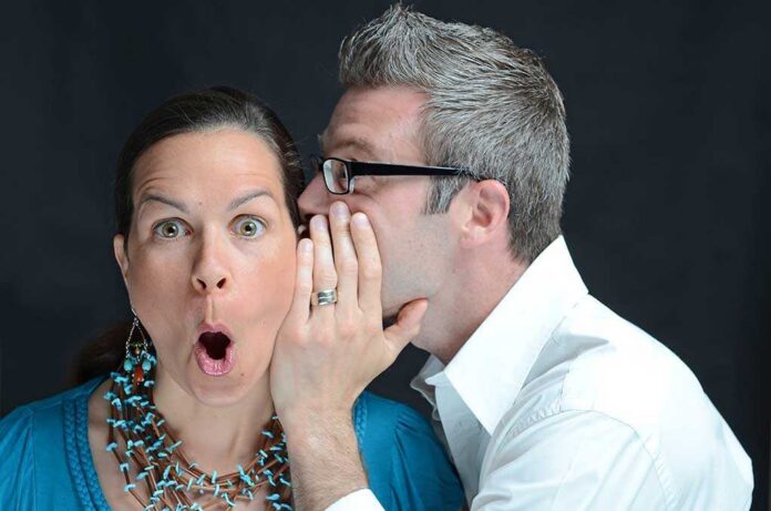 A surprised woman reacting while a man whispers in her ear