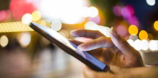 A persons hand using a smartphone in a city at night with blurred lights in the background