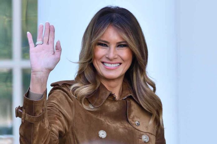 Melania Trump waving and smiling while wearing a stylish coat