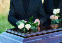 People placing white roses on a casket.