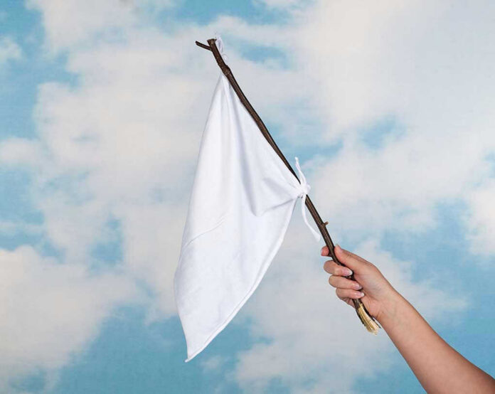 84861409 Hand holding white flag against a blue sky.