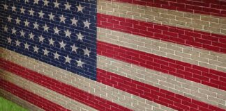 A man in a suit standing in front of a large American flag painted on a wall