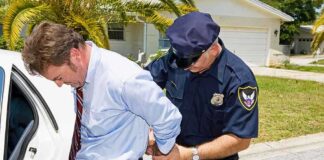 A police officer handcuffing a man in formal attire outside a police car