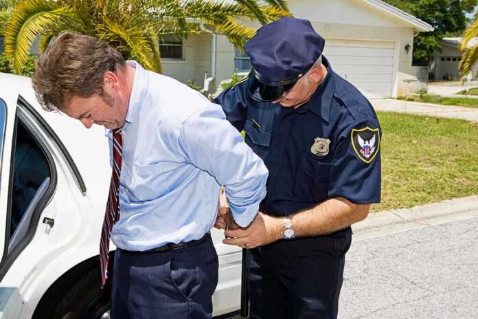 A police officer handcuffing a man in formal attire outside a police car