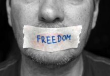 A mans mouth is covered with a piece of tape that has the word FREEDOM written on it