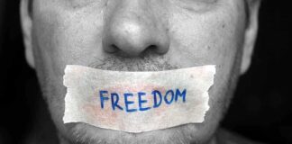 A mans mouth is covered with a piece of tape that has the word FREEDOM written on it