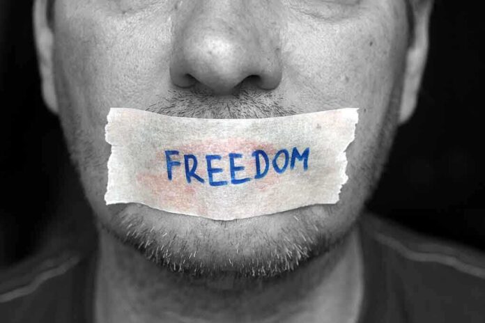A mans mouth is covered with a piece of tape that has the word FREEDOM written on it