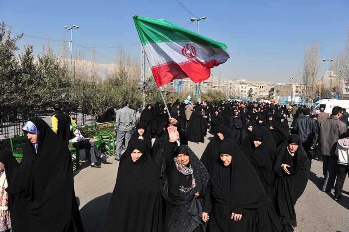 Group of women in black attire marching with an Iranian flag