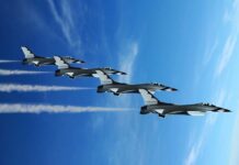 Four military jets flying in formation against a blue sky, leaving smoke trails