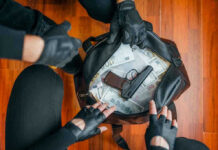 Gloved hands around bag with money and gun.