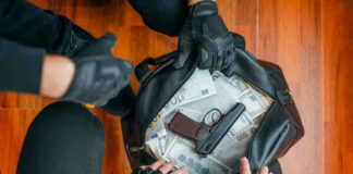 $1.8 Million Grabbed—Gone In Minutes Gloved hands around bag with money and gun.
