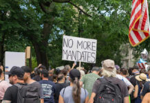 Crowd holds No More Mandates sign at protest.