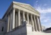 Exterior view of the Supreme Court building with columns and a statue of justice