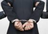 A person in a suit with hands cuffed behind their back