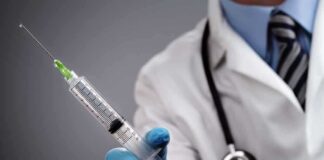 A doctor holding a syringe with a stethoscope around their neck